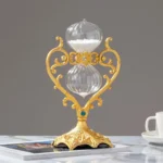 Decorative hourglass with a gold ornate frame and glass bulbs, placed on a white surface with a gray background.