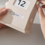 Vintage-style flip calendar showing the date "12" and the month "November" with a beige casing and manual adjustment knobs.