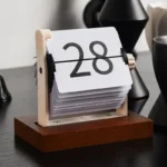 Flip calendar displaying the number 28 on a white card with black numbers, mounted on a wooden base.