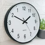 Quartz wall clock with black frame and white face, featuring clear black numerals and hands, ideal for educational or decorative purposes.