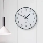 Simple round wall clock showing time at 10:09 with a white face and black numbers, ideal for modern home or office decor.