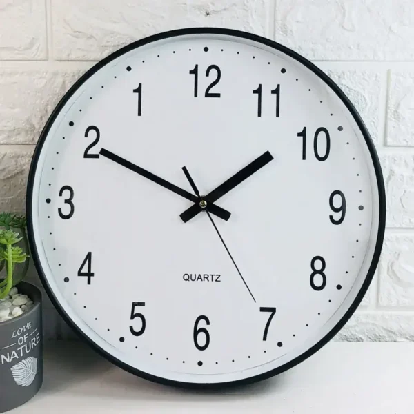 Round white quartz wall clock with black numbers and hands, showing time at 10:10, mounted on a white brick wall.