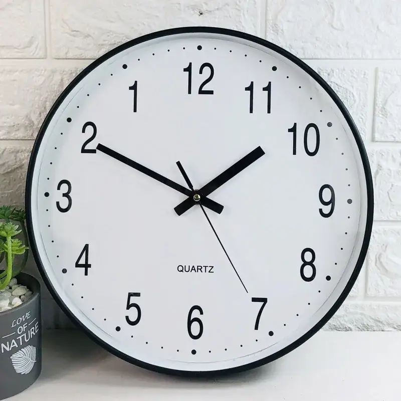 Modern Quartz Wall Clock for Home Decor Round white quartz wall clock with black numbers and hands, showing time at 10:10, mounted on a white brick wall.