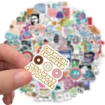 A close-up of a hand holding a sticker that reads "CUTE MECHANICAL ENGRAVER CUTE WORK FOR DONUTS" with images of donuts, set against a background of various colorful stickers.