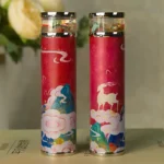 Two cylindrical herbal pill containers with colorful traditional Chinese art designs, featuring clouds, mountains, and a goat, used for storing herbal medicines.