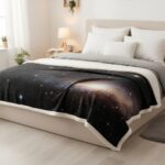Cozy bed with galaxy-themed blanket featuring stars and nebulae, in a modern bedroom setting.