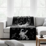 Soft throw blanket featuring a space-themed design with an astronaut, planets, and stars, perfect for decorating your living room or bedroom with a touch of outer space adventure.