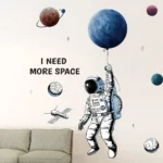 A space-themed wall decal featuring an astronaut holding a planet, with surrounding planets and stars, and the phrase "I NEED MORE SPACE" for educational or decorative purposes.