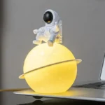 Cute astronaut figurine sitting on a glowing yellow planet lamp, perfect for space-themed decor and educational toys.