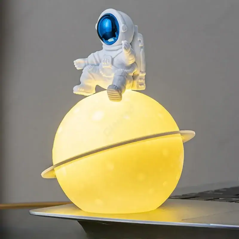 Space Explorer Astronaut Lamp with Planet Base Astronaut figurine sitting on a glowing yellow planet-shaped lamp with a ring, creating a space-themed decorative piece.