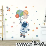 Fun space-themed wall decal featuring an astronaut holding balloons shaped like planets, with stars and a rocket, perfect for children's bedrooms or playrooms.