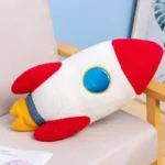 Soft rocket-shaped plush toy with red, white, blue, and yellow colors, designed for children and educational play. Perfect for science-themed decor and learning activities.
