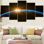 Multi-panel wall art depicting sunrise over Earth, hung above a white sofa with colorful cushions in a modern living room.
