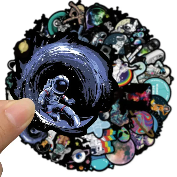 Hand holding a sticker of an astronaut floating in space with a swirling galaxy background, part of a collection of science-themed stickers.