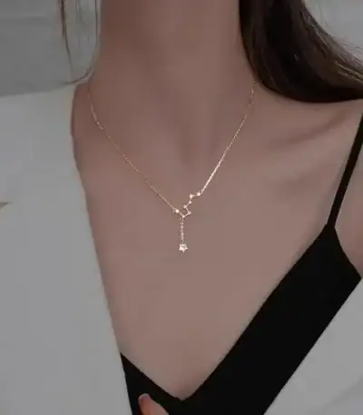 Close-up of a delicate gold necklace featuring a star-shaped pendant, worn by a woman with a black top and white blazer, highlighting stylish jewelry for women.