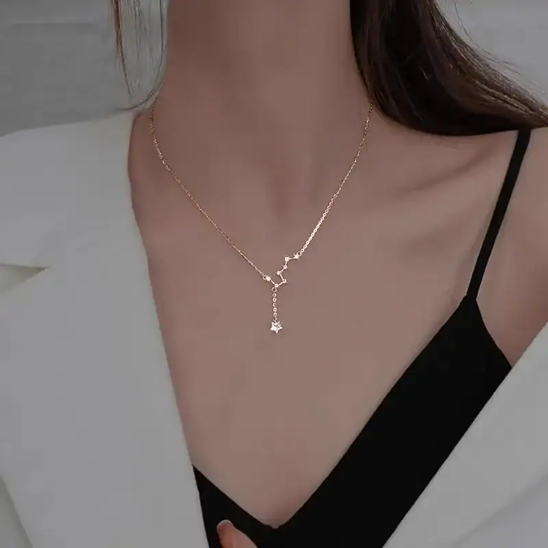 Close-up of a delicate gold necklace featuring a star-shaped pendant, worn by a woman with a black top and white blazer, highlighting stylish jewelry for women.