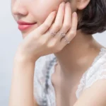Close-up of a woman's hand wearing multiple silver rings with small gemstone accents, resting gently on her face.