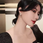 Elegant woman with dark hair and red lipstick, wearing a black sparkly dress and moon-shaped earrings, posing indoors.