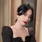 Elegant woman with short black hair and red lipstick, wearing a black sparkly dress, posing indoors.