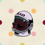 Enamel pin featuring a Soviet cosmonaut helmet with a detailed red bear face inside, symbolizing space exploration and Soviet heritage.