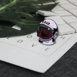 A detailed enamel pin featuring a bear wearing a space helmet with "CCCP" written on it, placed on a word game sheet with white tiles and green leaves in the background.