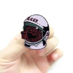 Close-up of a pin featuring a bear's face inside a space helmet, with "CCCP" written on the helmet, held by a person's hand.
