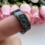 Black resin ring with colorful glitter particles embedded inside, designed for science-themed jewelry.