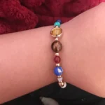 A vibrant beaded bracelet featuring planet and space-themed charms, including a gold ring, colorful beads, and planetary designs, worn on a wrist.
