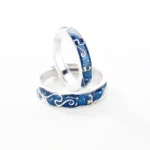 Pair of silver wedding rings with blue and gold wave patterns, symbolizing love and unity.