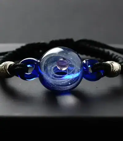 Elegant black cord bracelet featuring a central blue glass bead with swirling patterns and metallic accents, perfect for science-inspired jewelry enthusiasts.