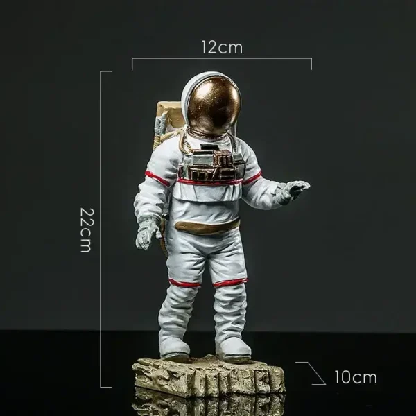 Astronaut figurine with a gold helmet, white suit with red accents, standing on a textured rock base, measuring approximately 22cm tall, 12cm wide, and 10cm deep.