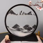 A circular decorative wall art piece featuring a monochrome mountain landscape with layered peaks and a serene lake, complemented by a cherry blossom branch.