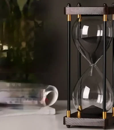 Stylish glass hourglass timer with black sand, featuring a wooden and metal frame, ideal for educational and decorative purposes.