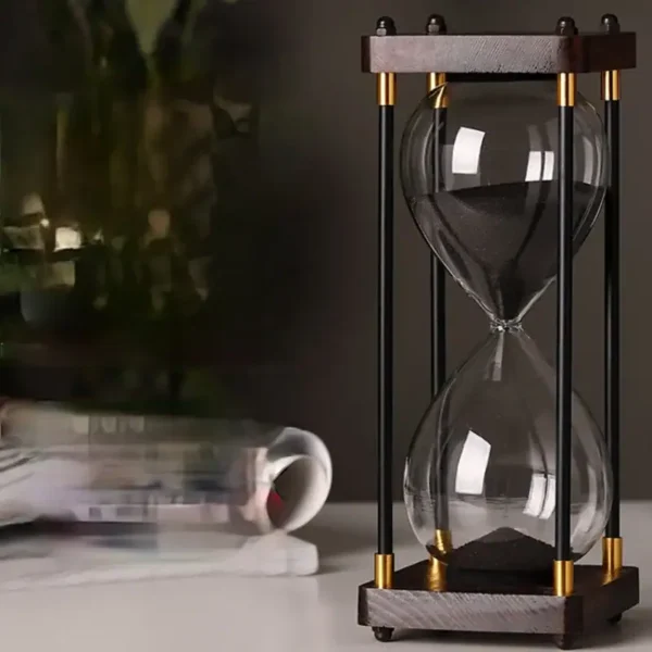 Stylish glass hourglass timer with black sand, featuring a wooden and metal frame, ideal for educational and decorative purposes.