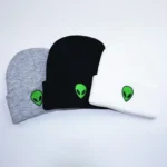 Set of three beanie hats in gray, black, and white, each featuring a green alien head logo, perfect for casual wear and sci-fi enthusiasts.