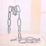 A contemporary sculpture made from interconnected metal chains, resembling a minimalist abstract figure, displayed indoors with soft natural lighting.