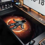Astronaut toy figure floating in space on a digital desk with a glowing orange background, surrounded by tech gadgets and a computer monitor, creating a futuristic and educational scene.