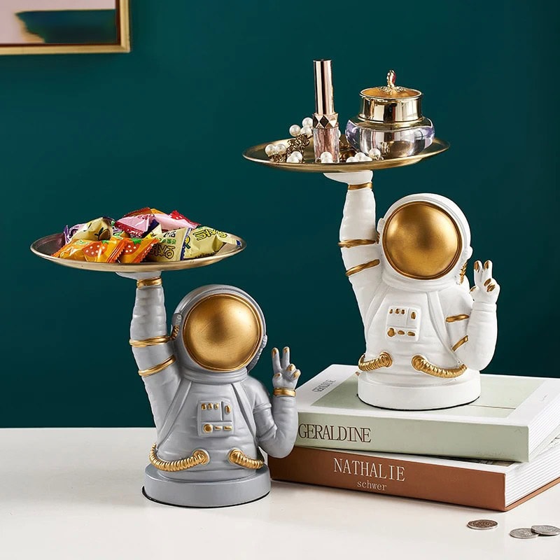 Space-themed astronaut figurines holding trays of candies and jewelry, decorative and educational for kids. Astronaut figurines with gold accents holding trays of candies and jewelry, perfect for science decor and educational toys.