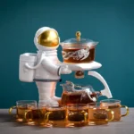 Space-themed tea set featuring an astronaut figure holding a tray with a glass teapot and cups filled with tea, set against a teal background.