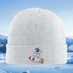 White knitted beanie hat featuring a cute astronaut robot riding a rocket, perfect for winter wear and space-themed fashion.