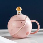 Pink space-themed mug featuring a cute astronaut lid with a gold helmet, decorated with stars and planets, perfect for science and space enthusiasts.