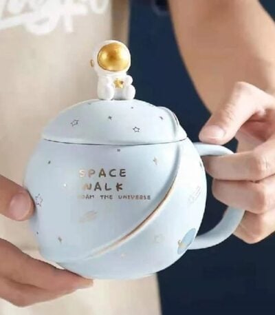 A ceramic mug designed with space-themed decorations, featuring a small astronaut figure on top and the words "Space Walk" on the side, perfect for science and space enthusiasts.