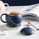 Blue celestial-themed coffee mug with matching mouse and spoon, featuring star and moon patterns, on a white surface with an open magazine in the background.