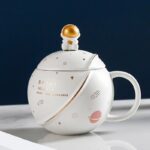 White ceramic space-themed mug with a planet-shaped lid and star patterns, perfect for science enthusiasts and space lovers.