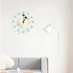A stylish mid-century modern wall clock featuring a white face with black hands and blue spherical accents, perfect for contemporary home decor.