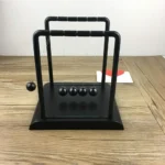 Classic black Newton's Cradle with five metal balls on a wooden surface, demonstrating conservation of momentum and energy in physics.