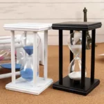 Two sand timers, one with blue sand and one with white sand, in black and white frames, ideal for educational demonstrations and home decor.