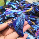 Hand holding a vibrant blue iridescent mineral specimen with a textured surface, surrounded by similar mineral pieces in the background.