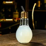 A creative light bulb-shaped liquid dispenser with a straw, placed on a wooden surface against a blurred cityscape background, perfect for science-themed decor or educational displays.