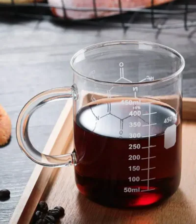 Beaker with dark liquid for science experiments, transparent glass with measurement markings, placed on a wooden surface.